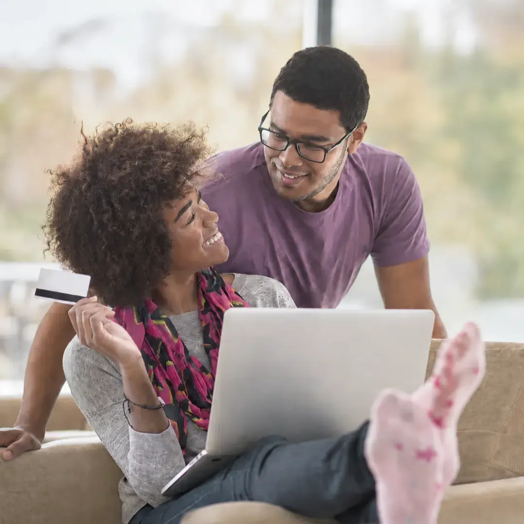 Happy couple using a laptop and credit card to easily book residential cleaning services online with Maryland Spotless.