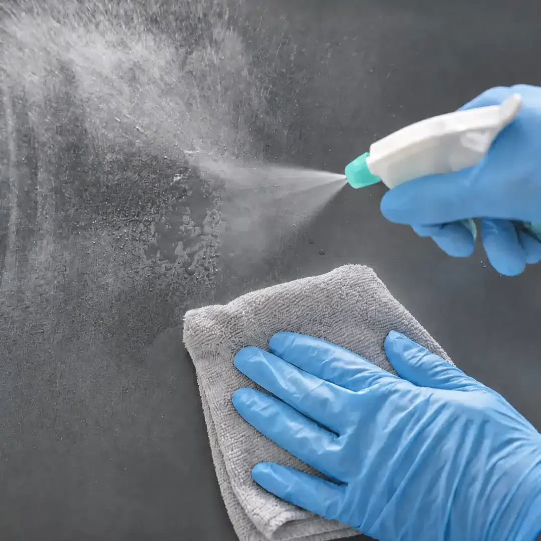 Professional cleaner wearing blue gloves spraying and wiping a surface, representing the detailed cleaning process.