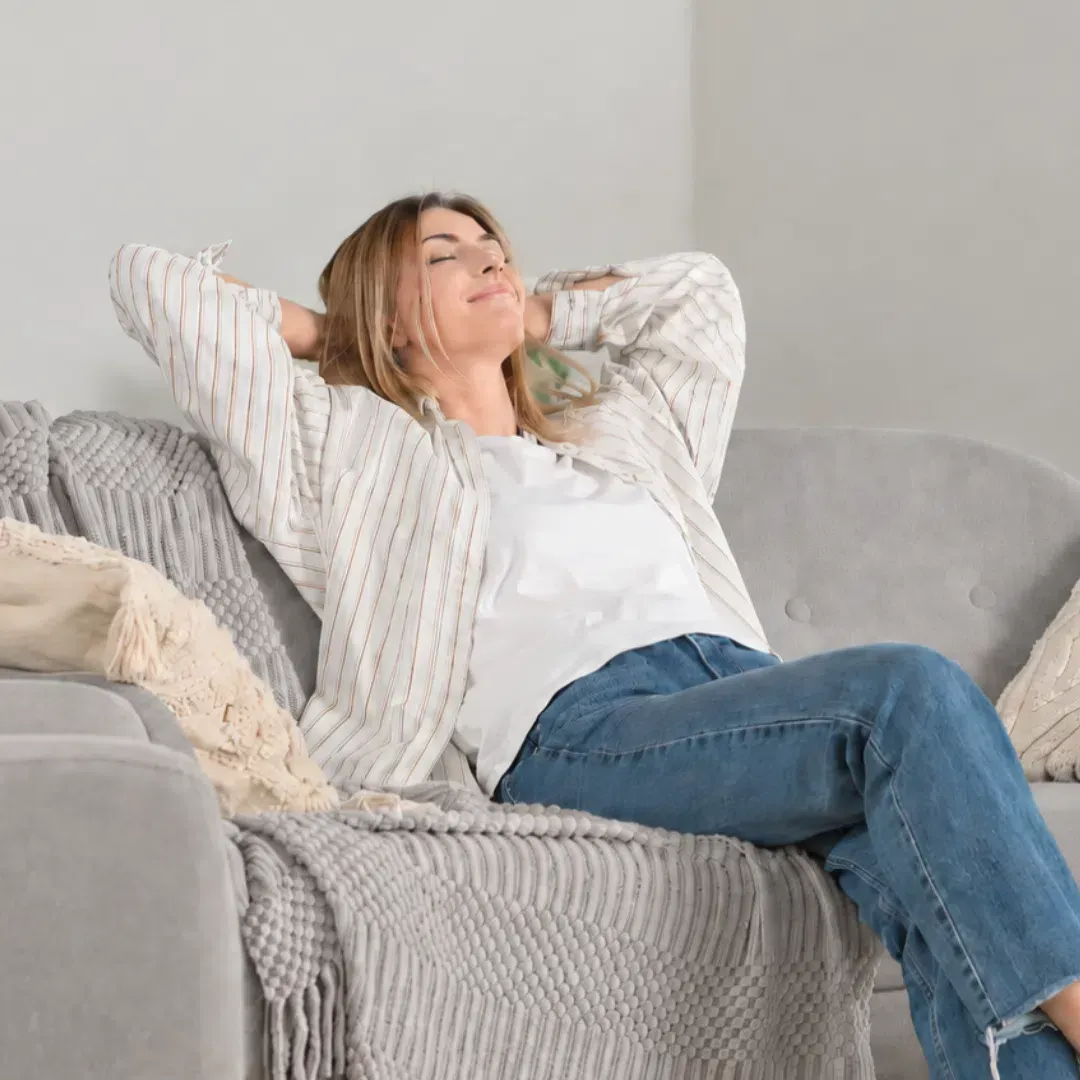 Smiling woman relaxing comfortably on a couch in her freshly cleaned home after using Maryland Spotless Maid Service.