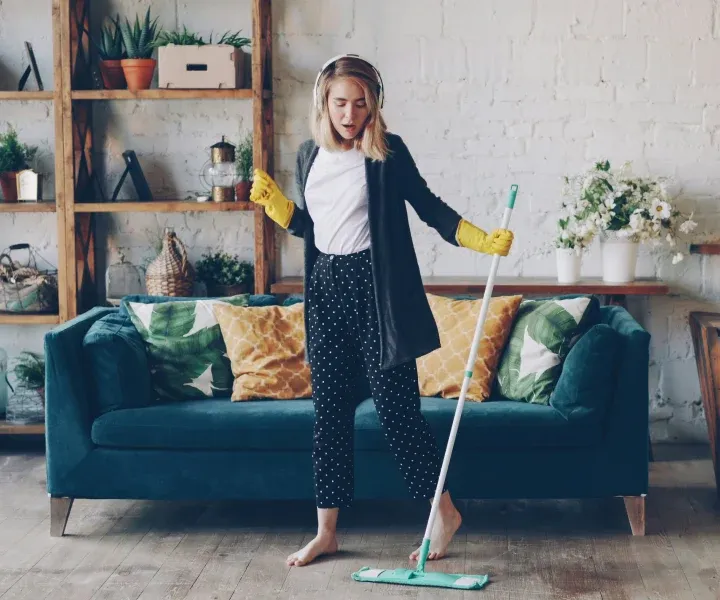 A background-checked professional cleaner wearing yellow protective gloves and happily mopping hardwood floors during a standard house cleaning service in Bethesda, MD.