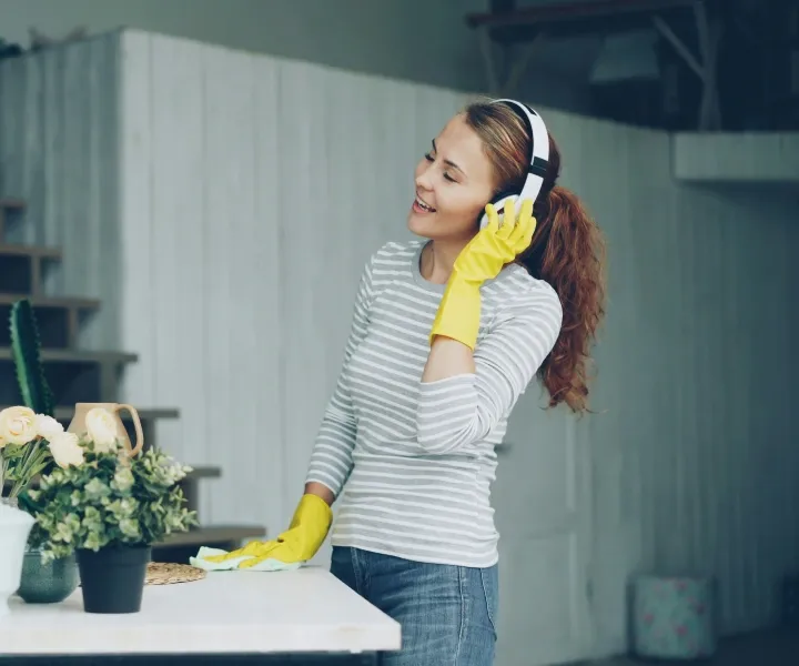 A background-checked cleaner from Maryland Spotless Maid Service wearing yellow gloves and headphones while wiping a white table during a house cleaning appointment in Rockville, MD.