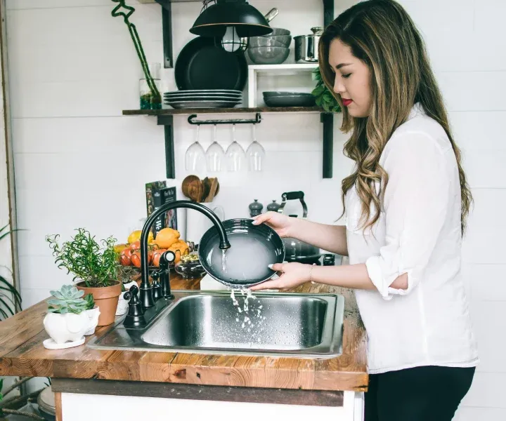 A background-checked professional cleaner from Maryland Spotless Maid Service washing and detailing a stainless steel kitchen sink in Germantown, MD.