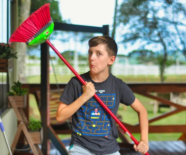 A young boy holding a red broom and smiling in a freshly cleaned, dust-free home in Germantown, MD, maintained by Maryland Spotless Maid Service.