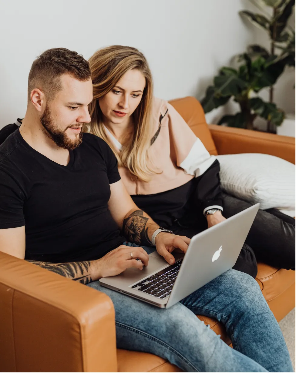 Couple sitting on a couch together, using a laptop to access online relationship support resources.