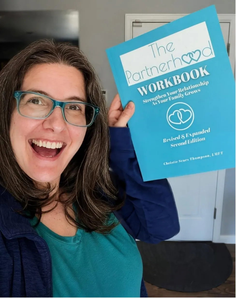 Christie Sears holds a bright blue book titled "The Partnerhood WORKBOOK: Strengthen Your Relationship As Your Family Grows."