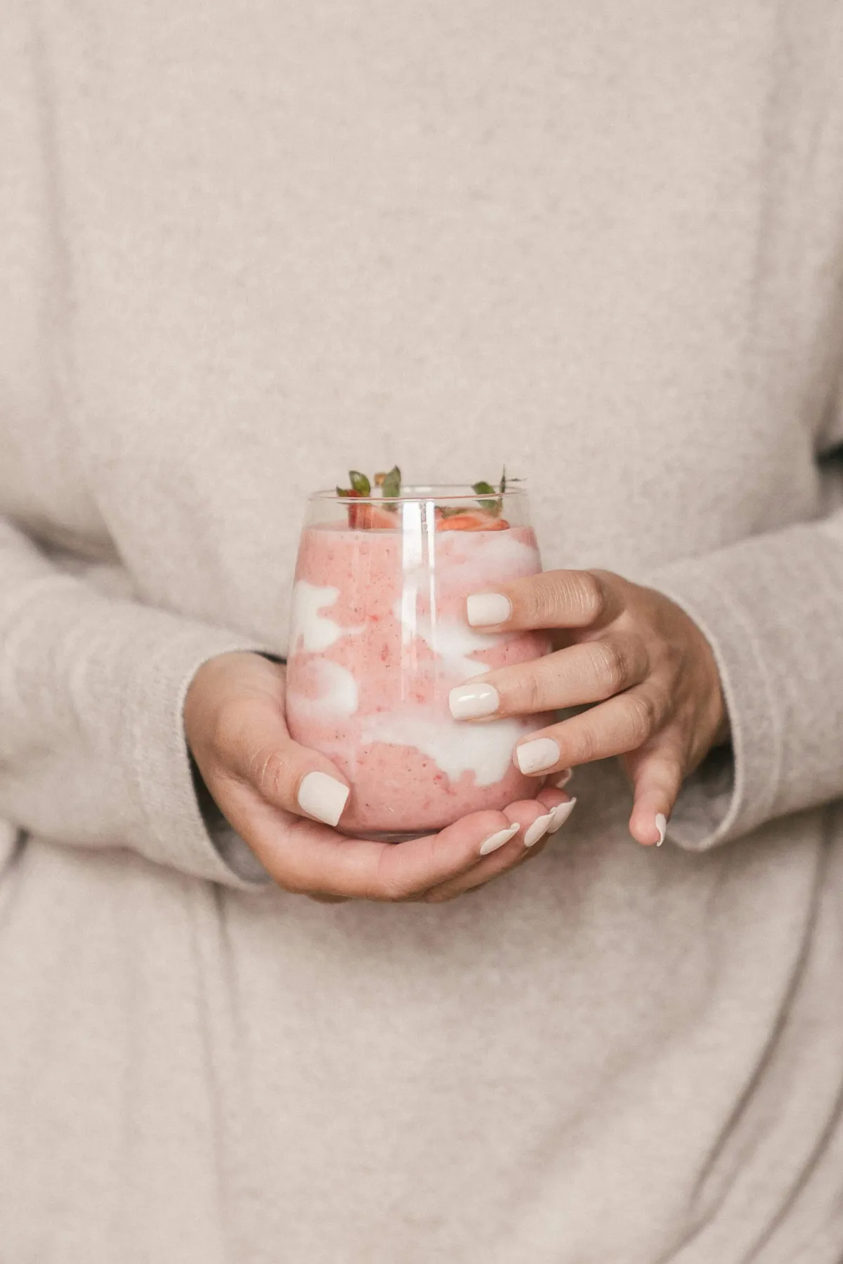 Handen die een glas met aardbei-yoghurt of smoothie vasthouden, als symbool voor gezond en bewust eten
