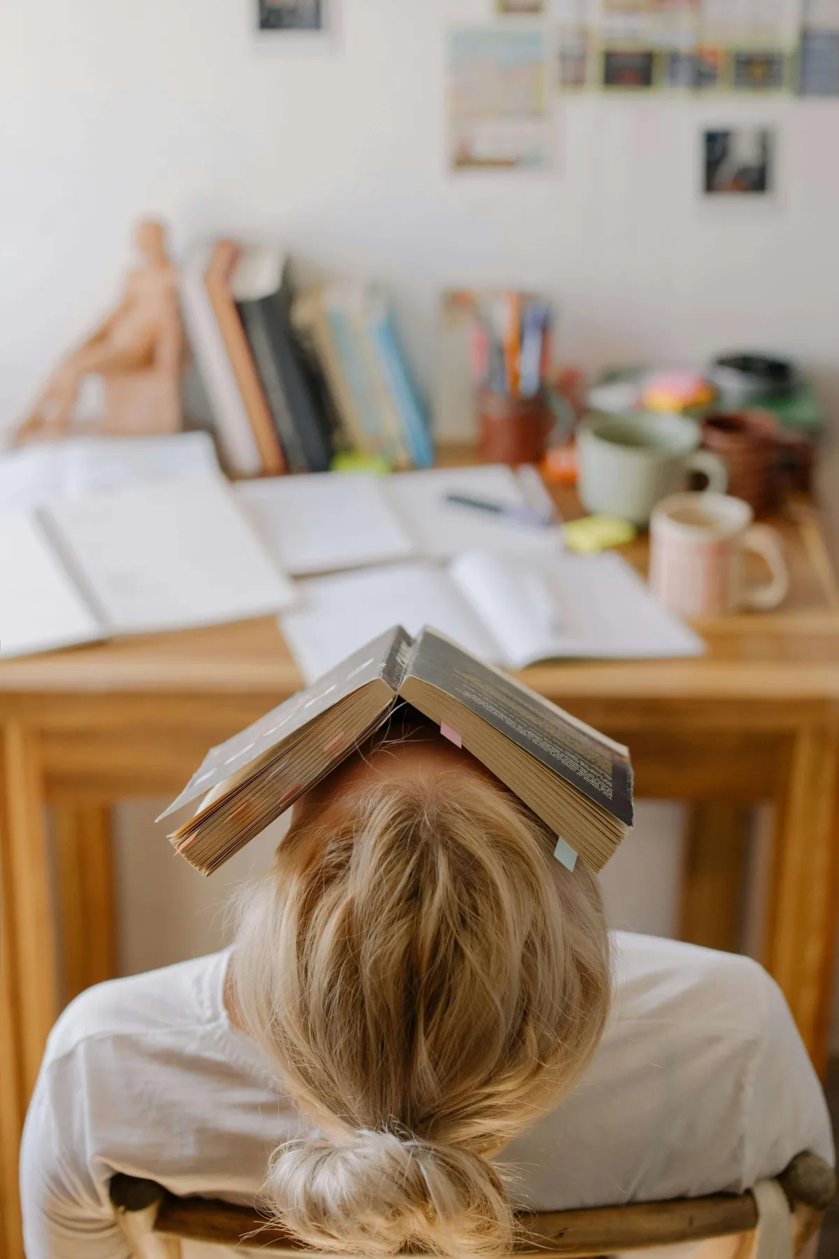Oververmoeide vrouw met boek op haar hoofd als uiting van stress tijdens het studeren of werken