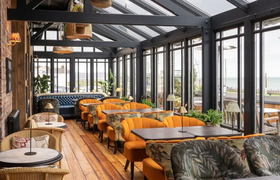 A pastel-hued event scene at Blossom Hall featuring women attendees in soft pastel outfits, with soft sunlight and blooming gardens.