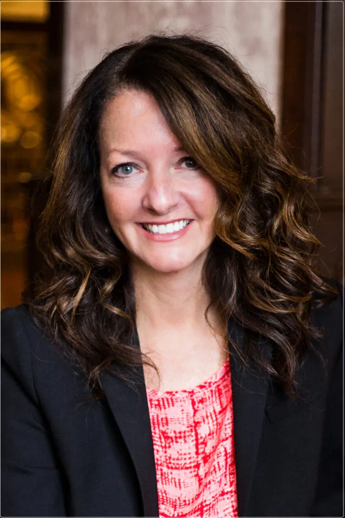 Portrait photo of a smiling woman with wavy dark hair wearing a black jacket.