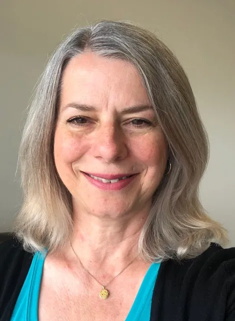 Portrait photo of a smiling woman with silver hair wearing a dark jacket over a blue top.