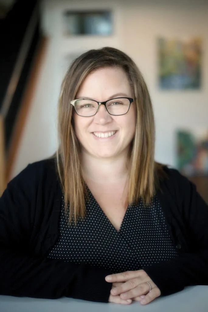 Portrait photo of a smiling woman with glasses and dark hair wearing a black top.