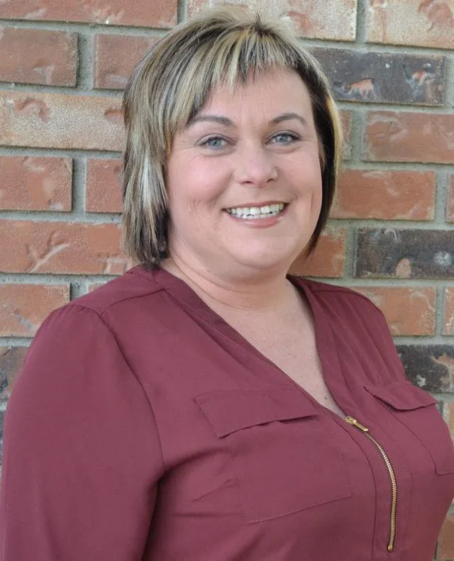 Portrait photo of a smiling woman with short blonde hair wearing a maroon top.