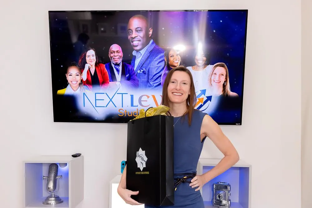 Jennifer Licciardi smiling and holding a gift bag in front of a sign that reads “Next Level.”