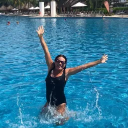 Kerri Spencer, hairstylist and Monat representative is in a beautiful blue swimming pool, wearing a black one piece swimsuit and sunglasses.