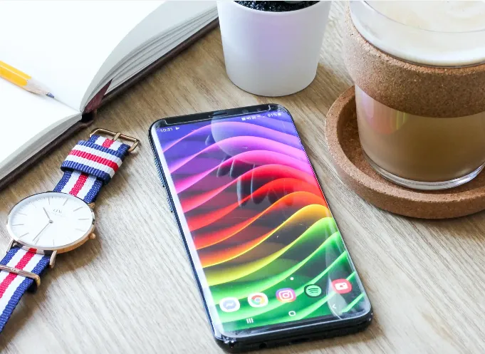 Smartphone resting on an open notebook beside a pen, watch, and coffee mug on a desk