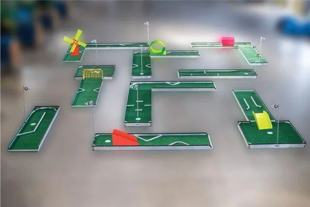 A couple enjoying a date night mini golf game under string lights in a cozy indoor venue. The portable course features whimsical obstacles, and the couple is smiling as they compete playfully.