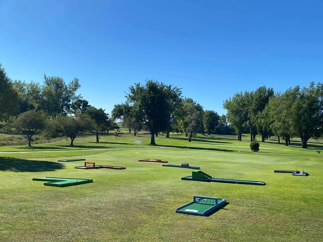 A retirement community event with seniors playing mini golf on a sunny patio. The group is engaged and laughing, with staff assisting and everyone enjoying the inclusive activity.