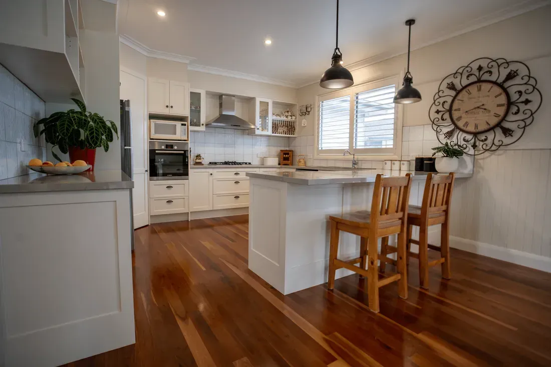 Elegant modern kitchen renovation in Aspendale by K2 Homes, featuring natural hardwood flooring matched with warm-toned dining chairs, minimalist cabinetry, and complementary lighting and wall accents