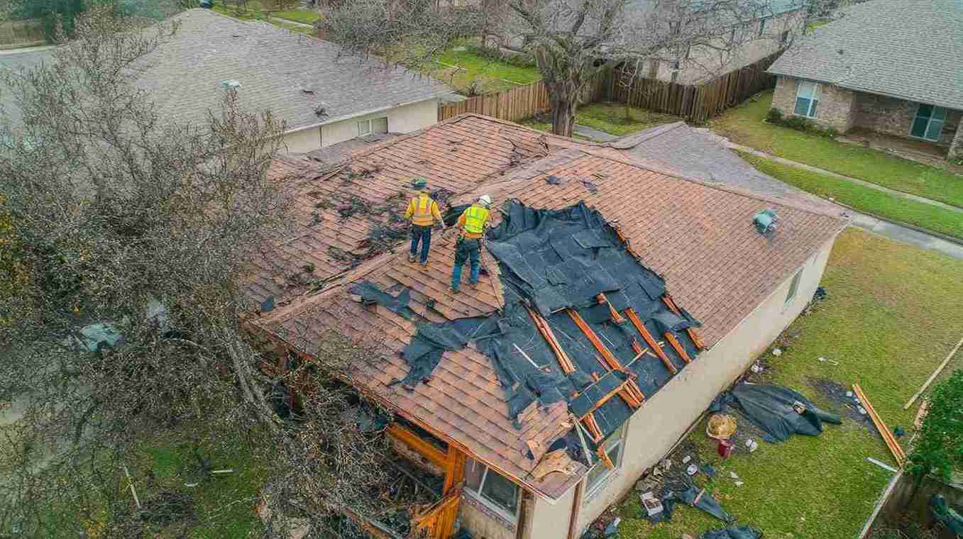 Roofers removing damaged shingles during residential roof replacement