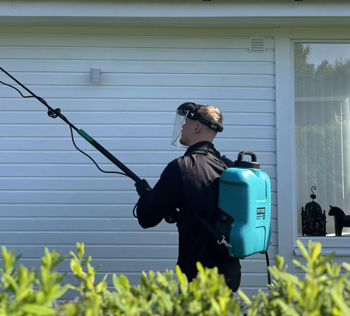 Medarbetare från Spindelmännen i arbetskläder framför en ljus fasad, fotografi i naturligt dagsljus, fokus på professionell utrustning och vänligt kroppsspråk för att kommunicera trygghet och kunnande.