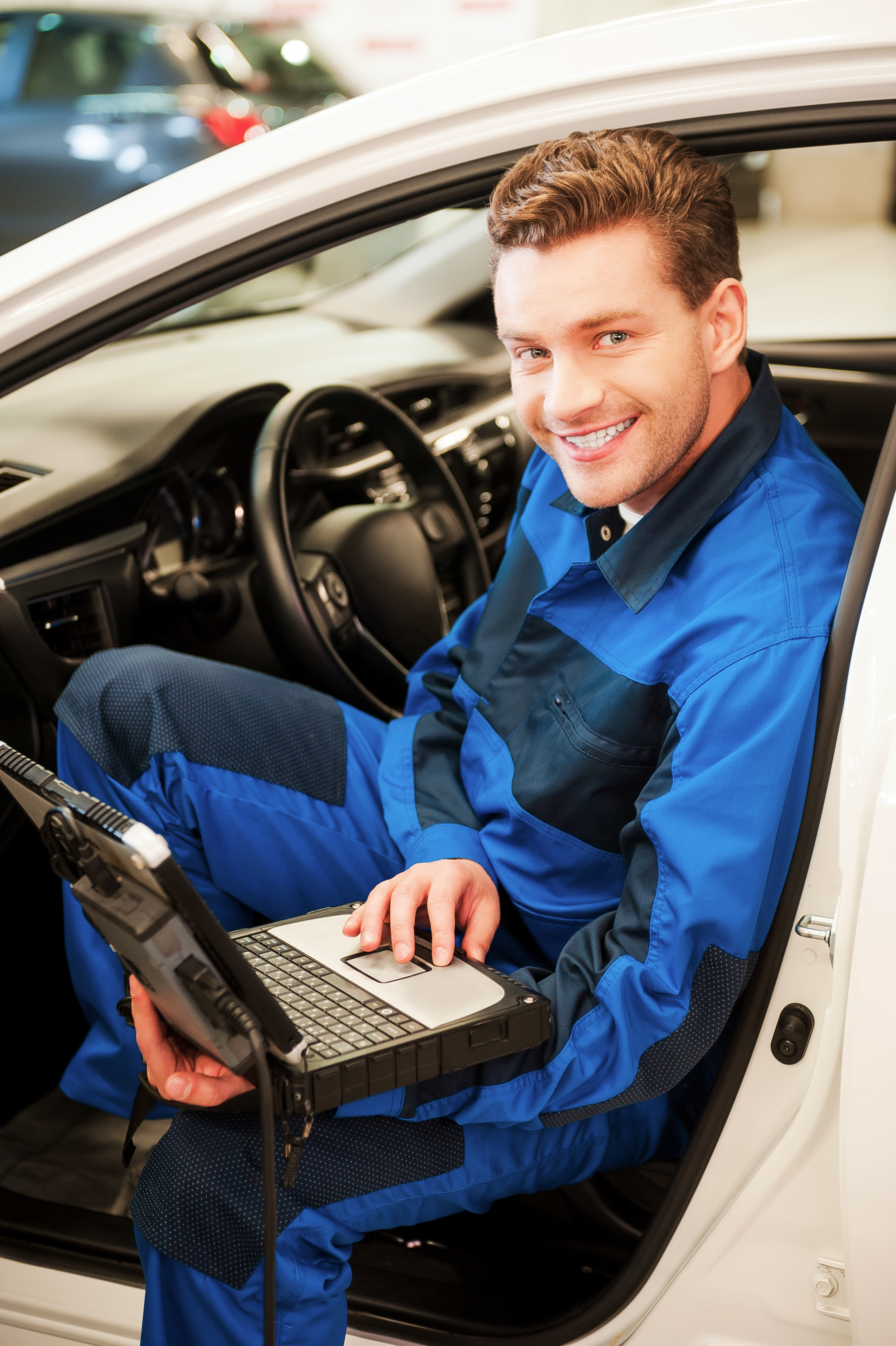 A mechanic kneeling beside a car in an Australian workshop, phone ringing on bench
