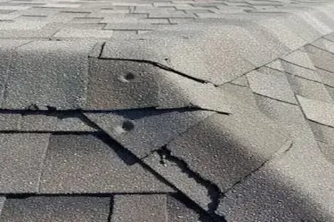 Cracked and splitting asphalt shingles with visible hail damage across the surface