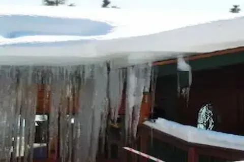 Large ice dam with heavy icicles hanging from snow-covered eaves on residential roof in Maple Grove
