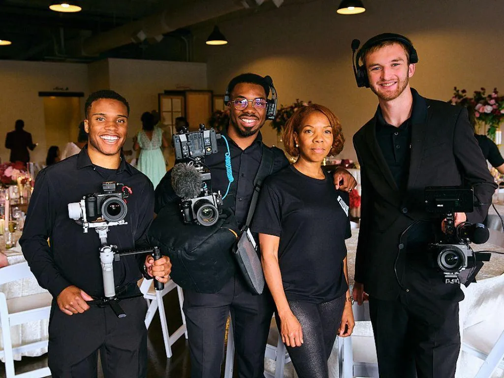 Wedding videographer filming at sunset with handheld camera; cinematic documentary style.
