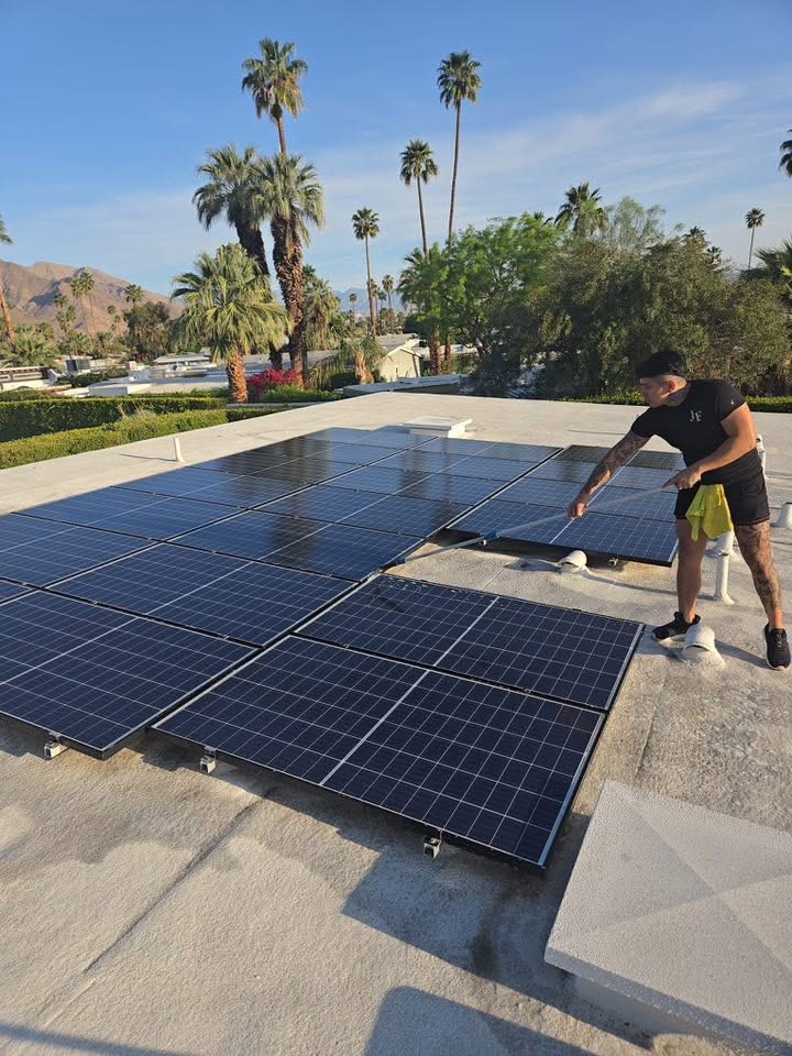 Technician cleaning solar panels on a rooftop with brush and water flow