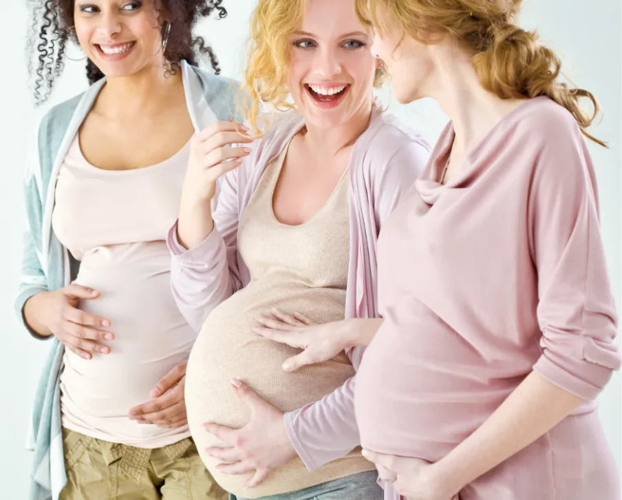 3 pregnant women smiling. Each holding their baby bump.