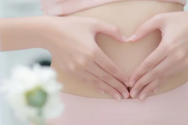 Hände formen ein Herz vor dem Bauch – Symbolbild Körperverbindung