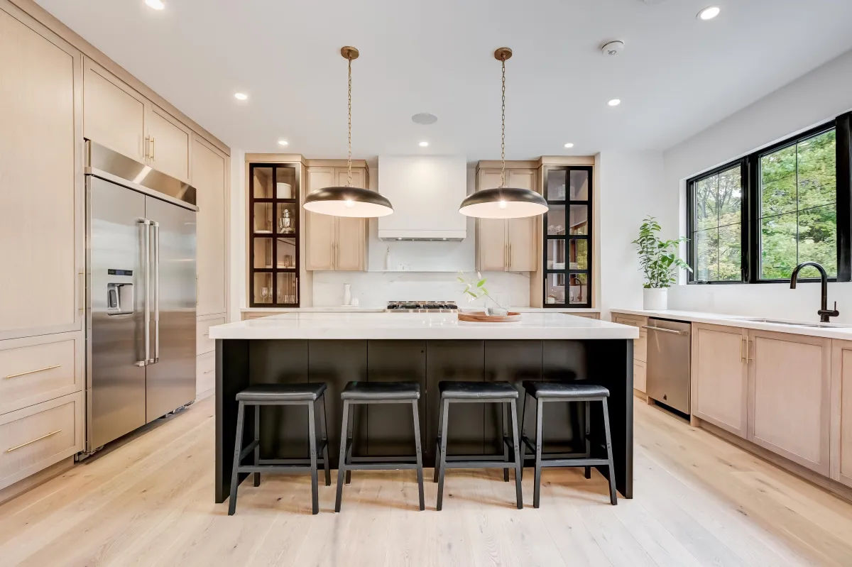Contemporary kitchen with light wood cabinets, white island, black bar stools, and double pendant lights.