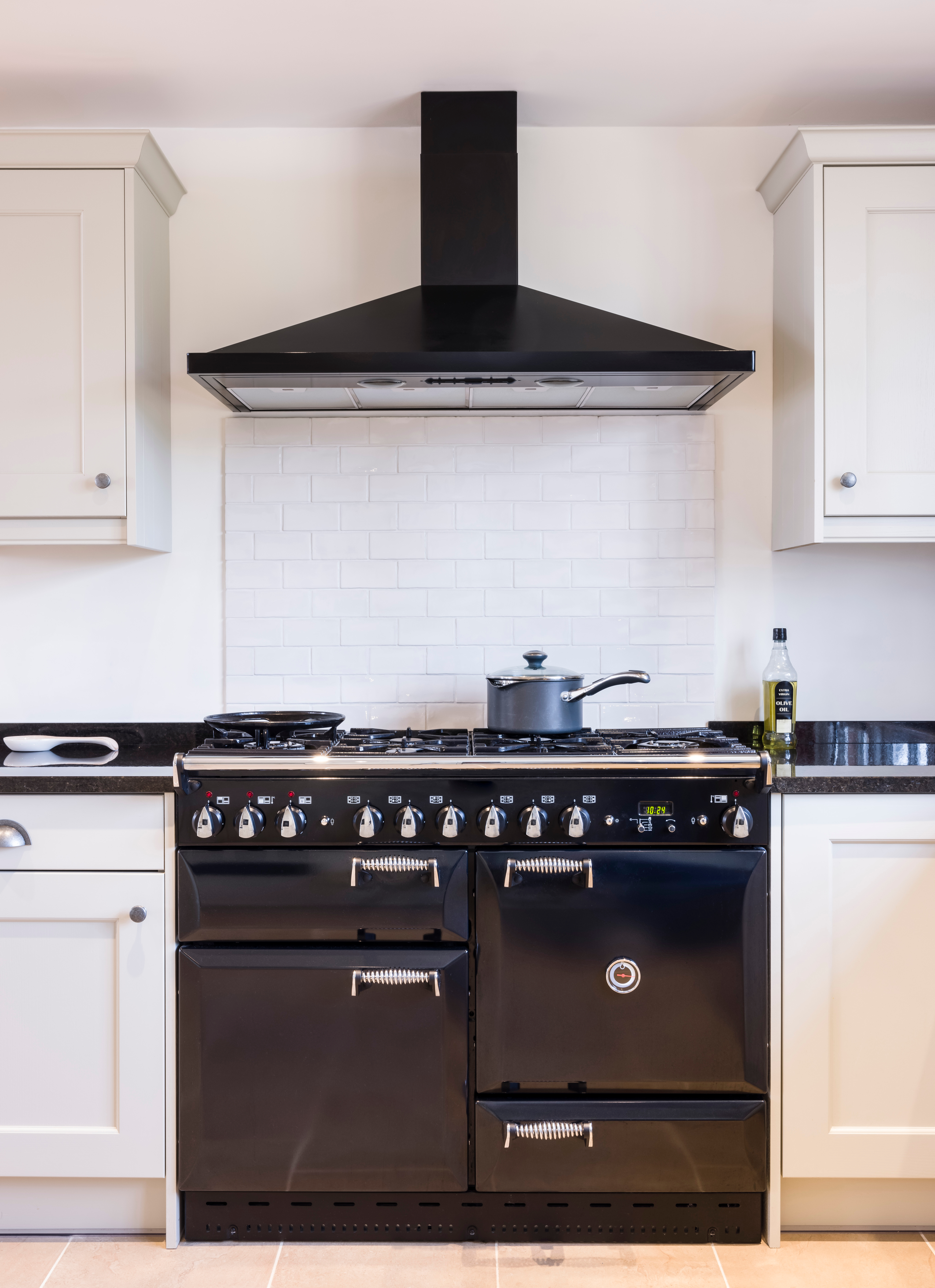 White kitchen with black range, white cabinets, and backsplash tile.
