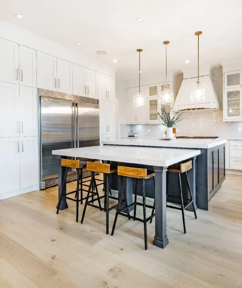 Modern white kitchen design with black island, pendant lights, and hardwood flooring.