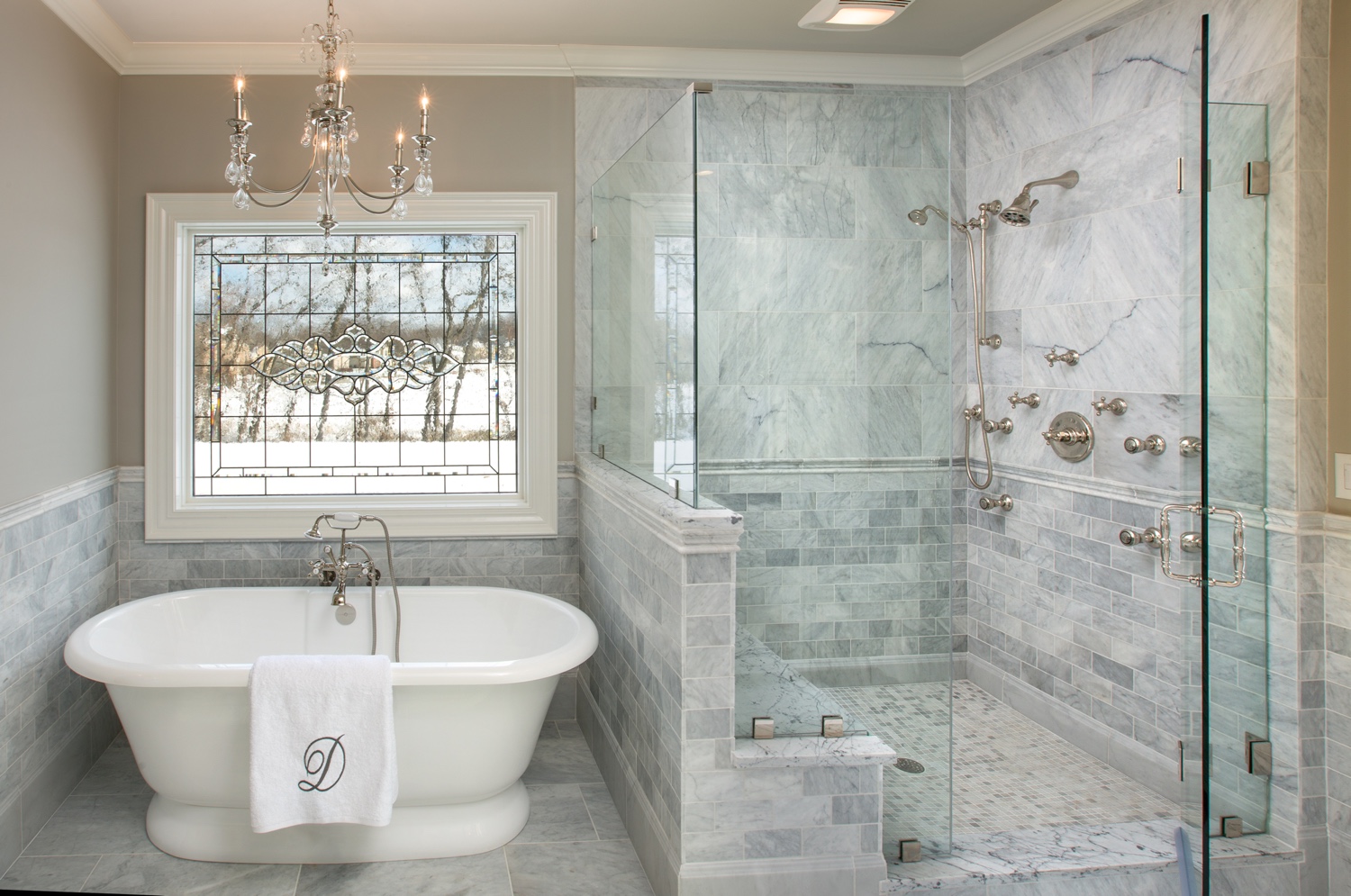 Walk-in shower with glass doors, bench seating, and patterned tile flooring.