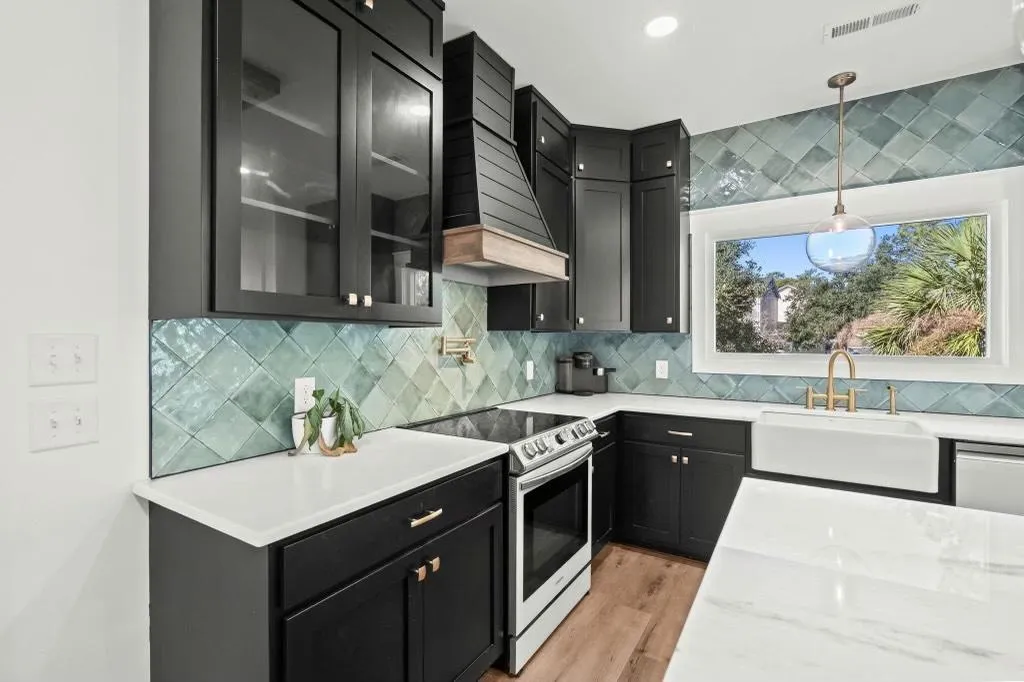 Remodeled kitchen with black shaker cabinets, teal tile backsplash, stainless steel range, and large picture window.