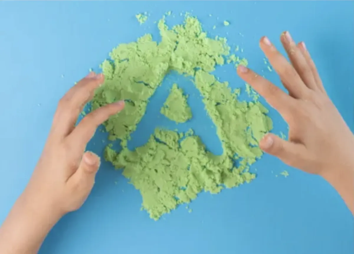 Child writes A in green sand