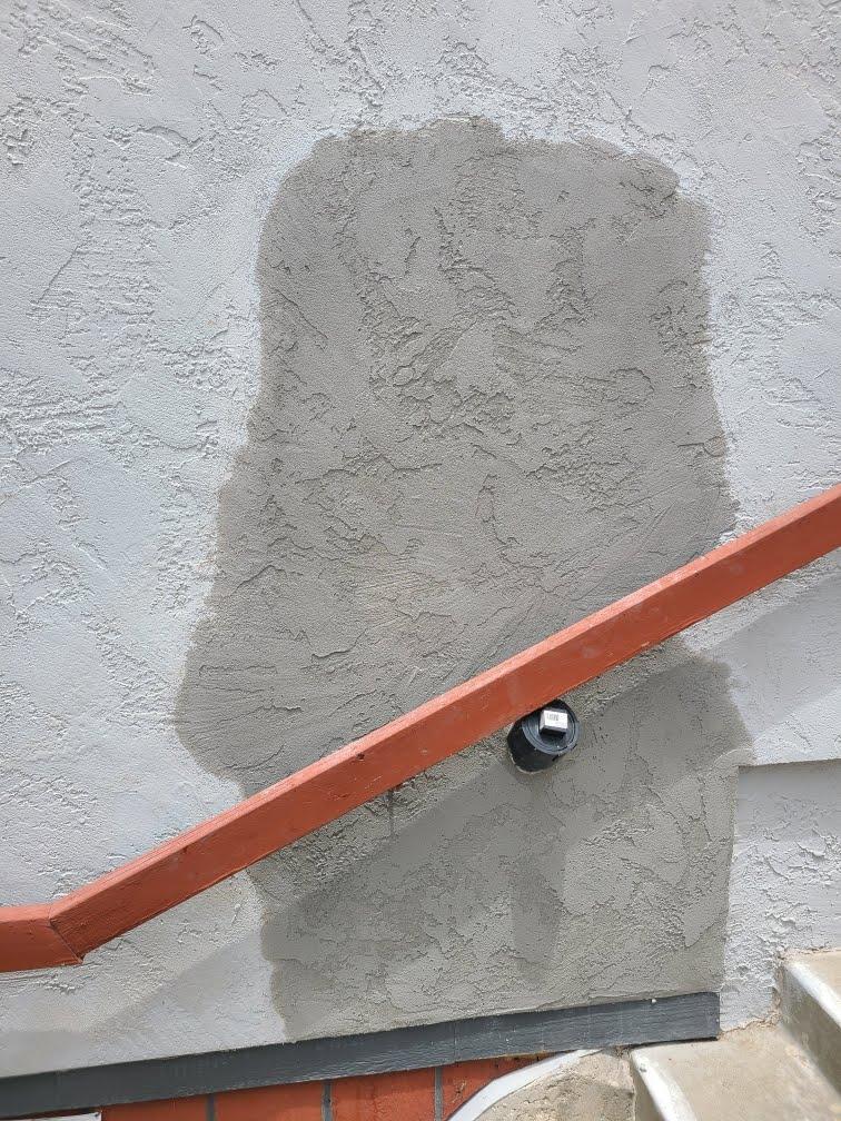 Stucco and plaster repair wall with red railing and patched surface