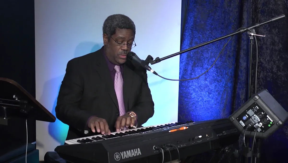 A close-up portrait of Morris Hunter, a mid-30s musician with expressive eyes, holding an acoustic guitar. The background is softly blurred, focusing attention on his thoughtful expression and creative spirit.