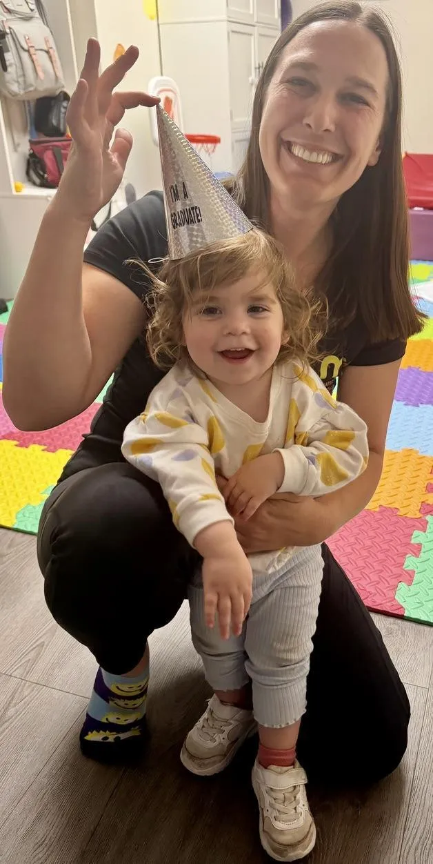 Child holding a "Way to Go!" certificate with a smiling therapist in a pediatric therapy setting, highlighting achievements in the Moving and Grooving PT program.