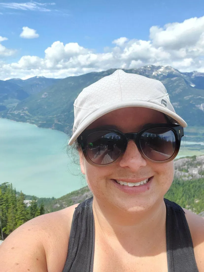 Woman smiling with sunglasses on, mountain and lake in the background 