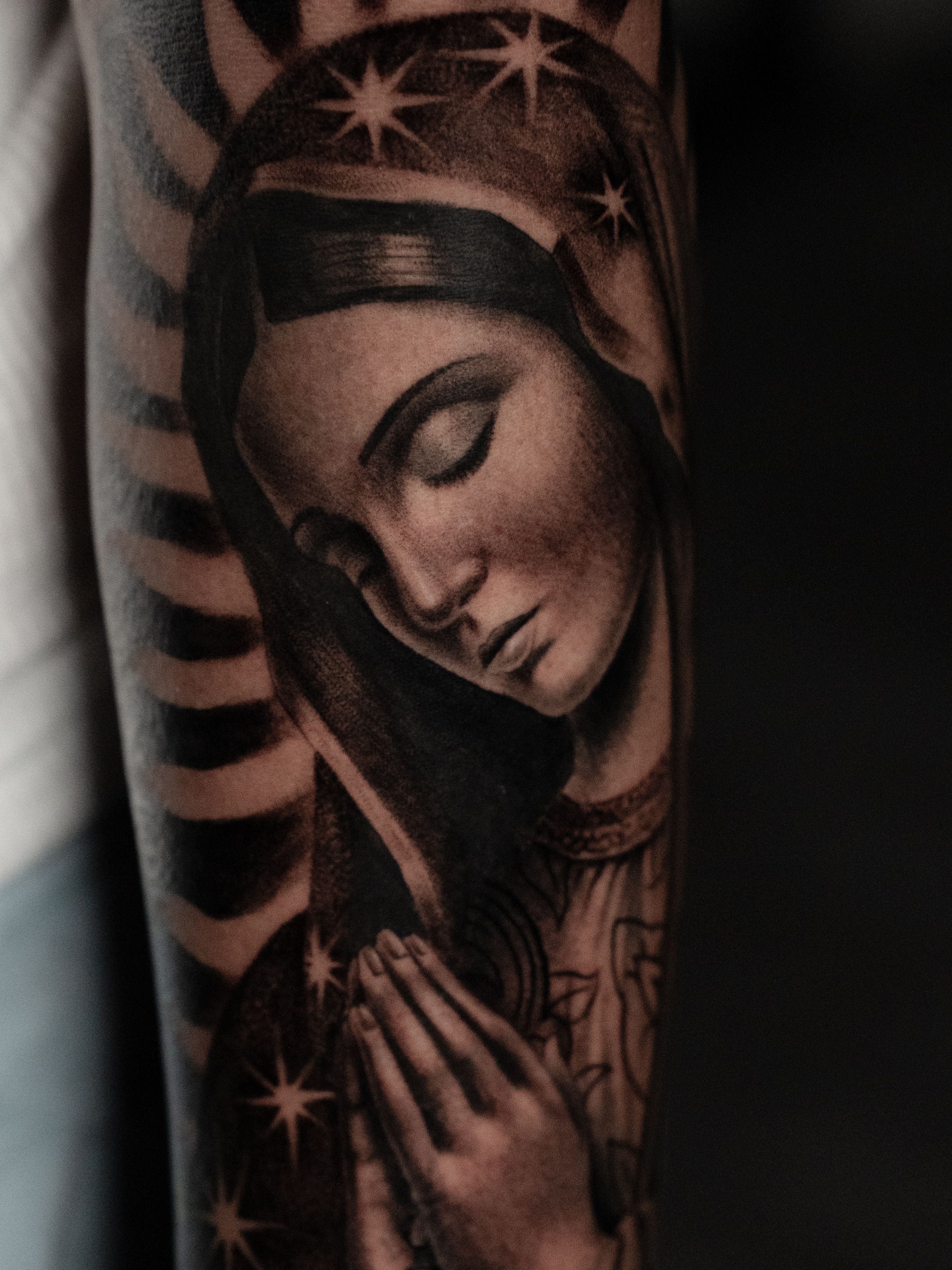 A delicate botanical tattoo wraps around a woman’s forearm, featuring fine line peonies and eucalyptus leaves. The design is minimalist, with subtle shading, and the photo is taken in natural daylight, emphasizing the softness and elegance of the artwork.