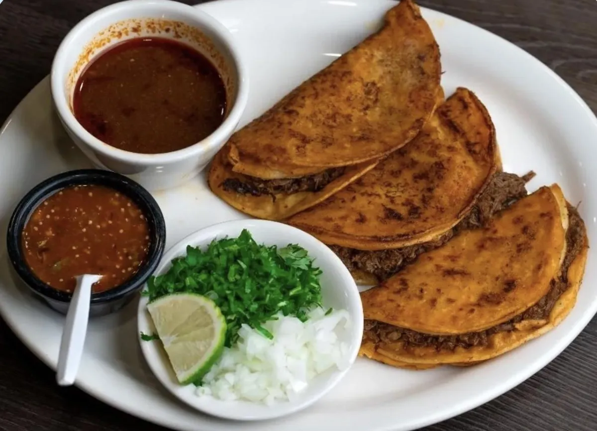 Close-up of a skillet of bright, sizzling tacos with charred corn tortillas, cilantro, and a lime wedge.