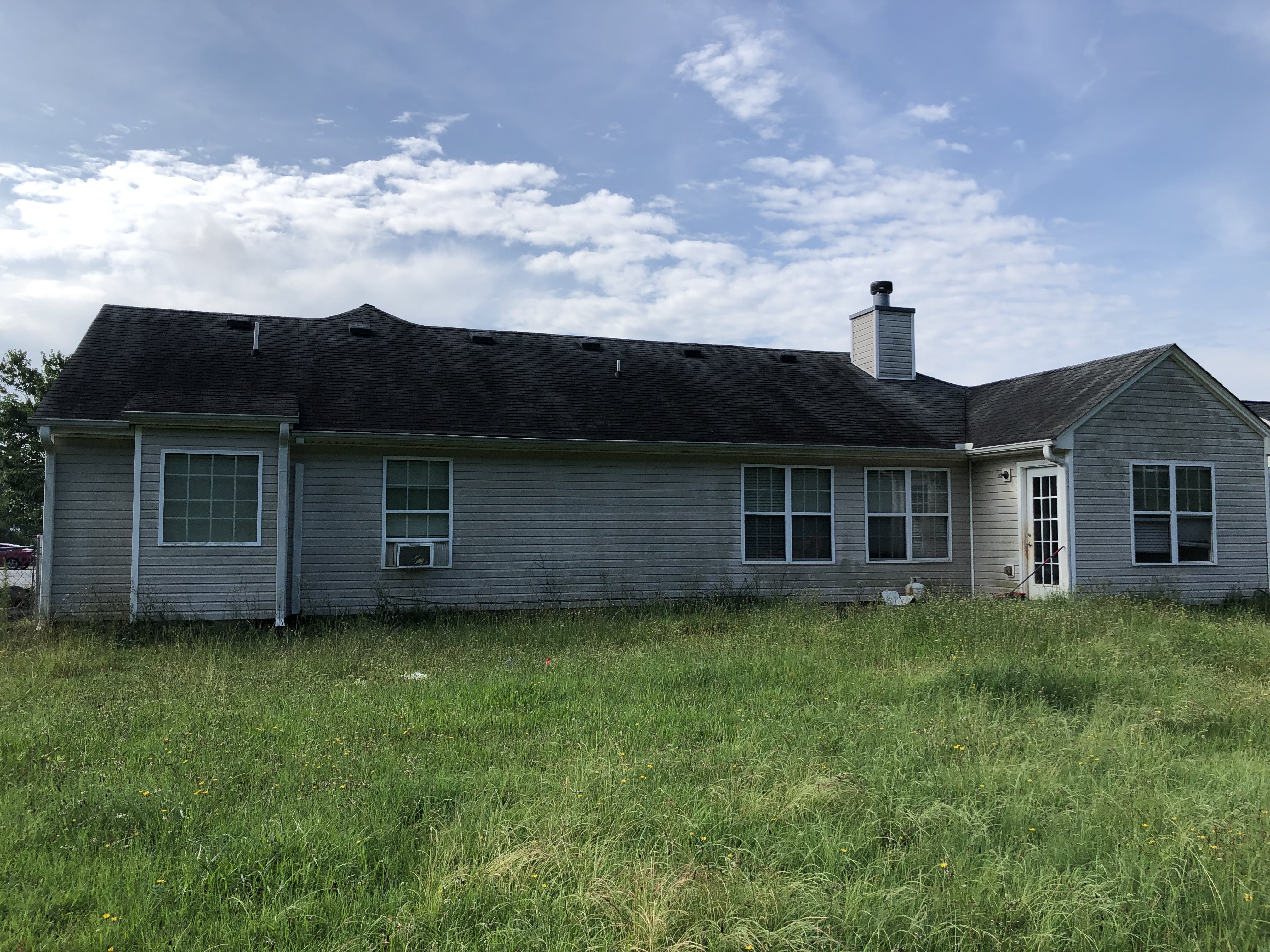 Sell My House As Is in Snellville. Back of vinyl house with dirty siding, overgrown yard, needs roof.