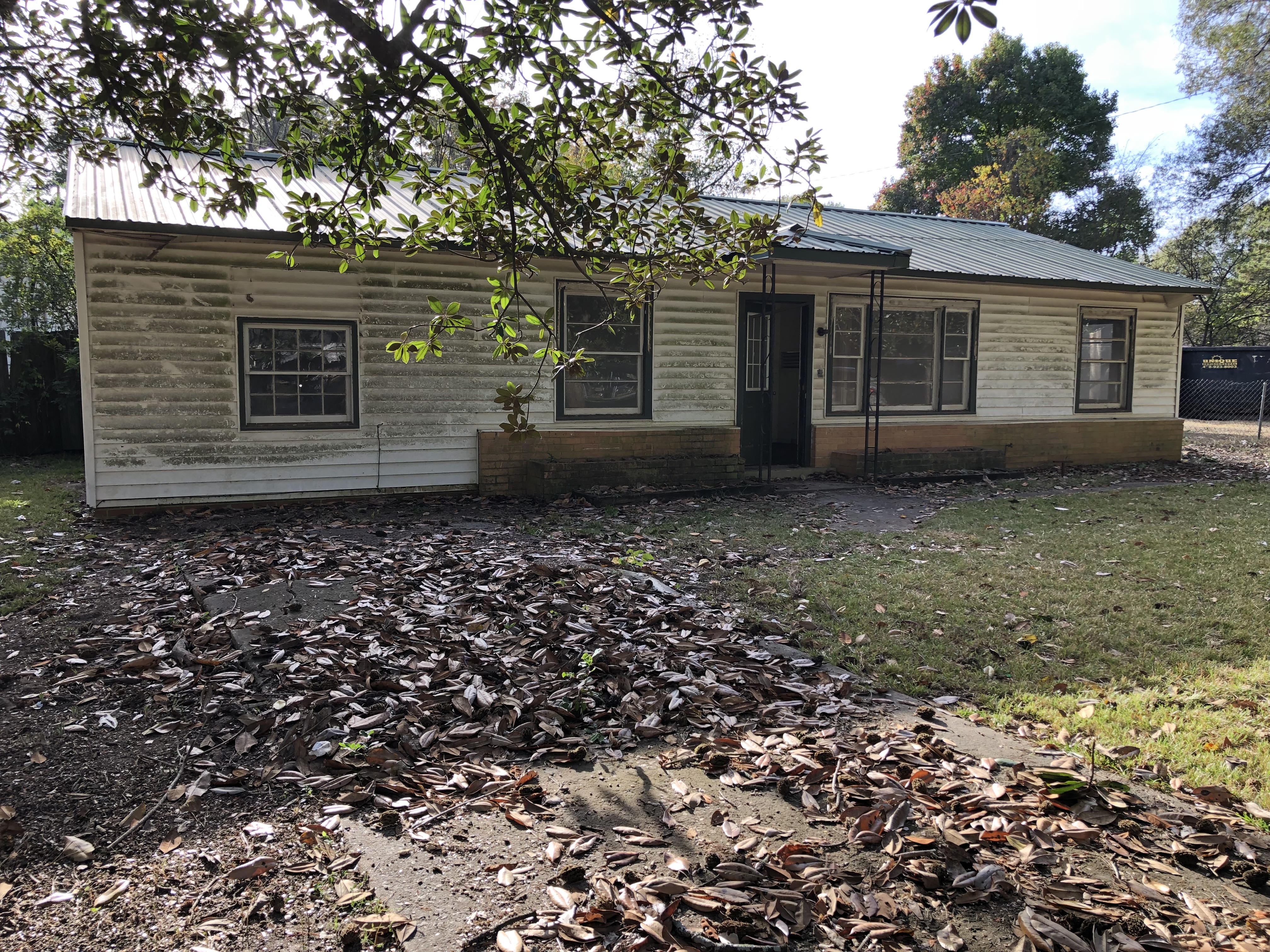 Damaged Vacant house. White vinyl one story home with green metal roof.