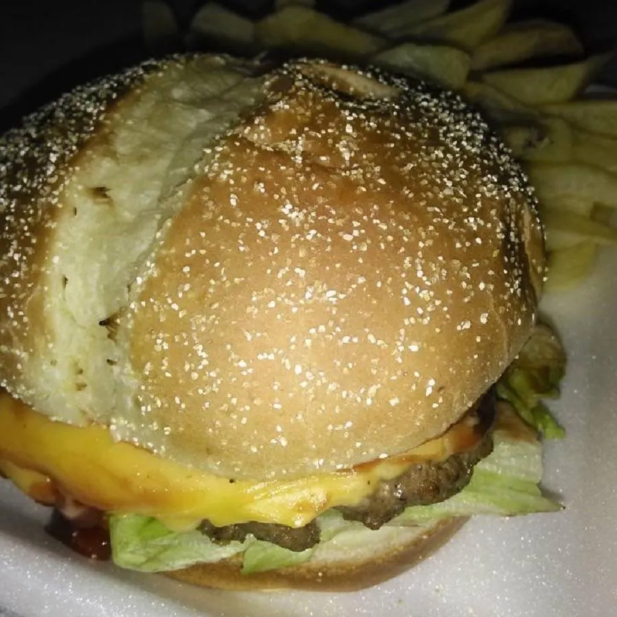 Close-up of a chargrilled burger with melted cheese, lettuce, tomato, and house sauce on a toasted bun, served on a wooden board.