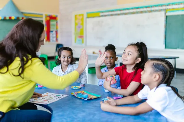 Primary school teacher engaging with diverse students in a classroom, promoting positive learning through interaction and encouragement.