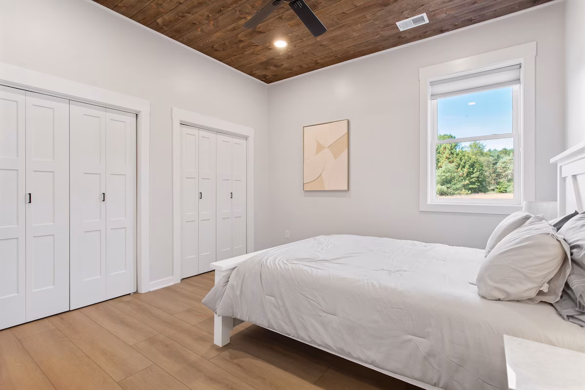 alternate view of bedroom showing window, ceiling fan, and closets.
