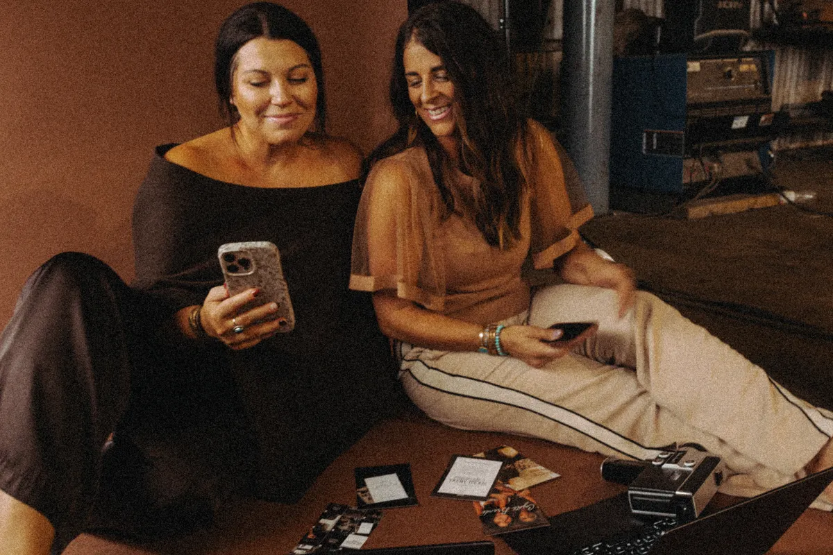 Courtney and Kori sitting on the studio floor, reviewing photos on a phone and prints