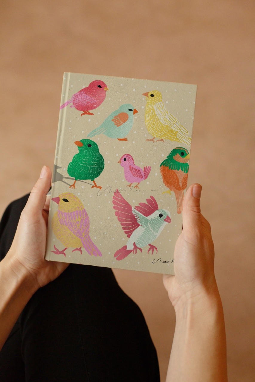 Woman holding a journal featuring the Flock Together bird illustration from a licensable surface pattern collection.